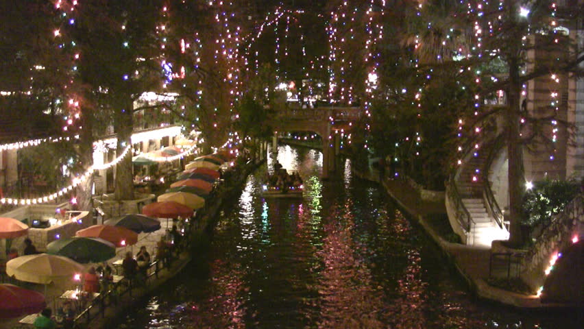 Video night Christmas lights of the San Antonio Texas Riverwalk. Tourists walking by restaurants and shops. Vacation area. Bright lights and festive holiday atmosphere. Foot bridge in distance.