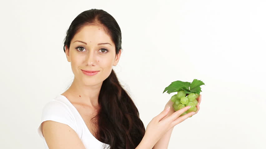Young attractive woman playing with and offering green grape cluster on white