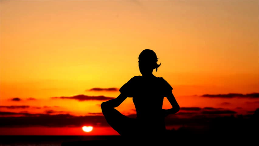 Silhouette of woman meditating during sunset