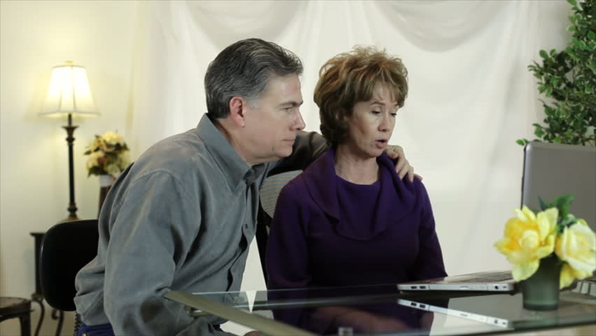 A mature couple sitting in front of a wireless laptop computer as the man instructs or teaches the woman how to use it without a mouse.
