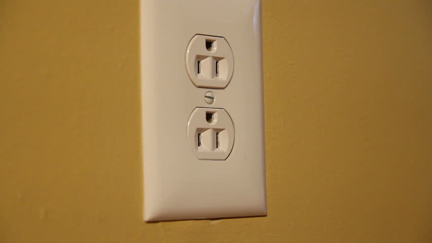 Close-up shot of a man plugging and unplugging an orange electrical cord into a U.S. wall outlet.