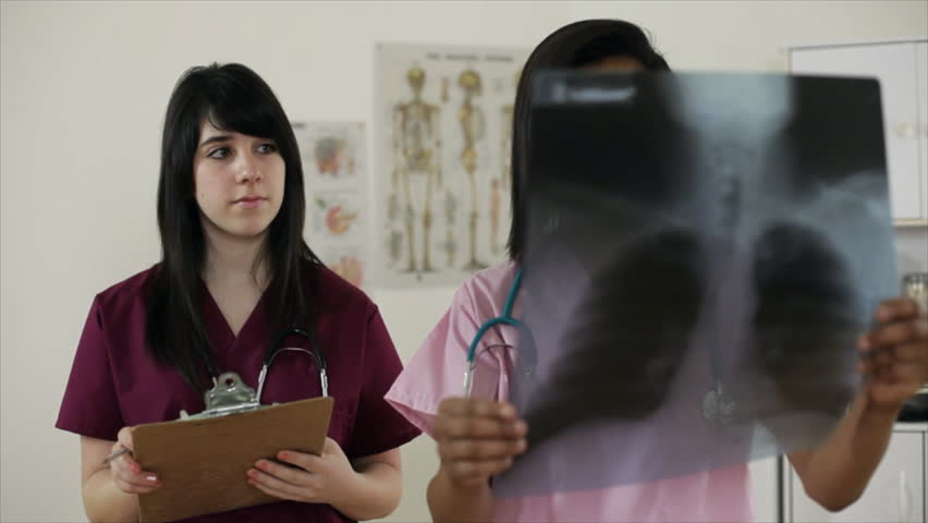 The camera dollies around from an x-ray film to reveal a lovely young African American nursing student discussing findings with a fellow nurse intern. Nurse holding x-ray is main focus. 
