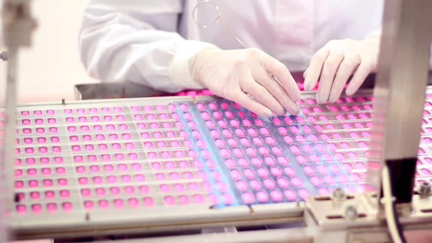 Worker manually puts pills in empty containers as they move along the conveyor belt. HD 1080p.