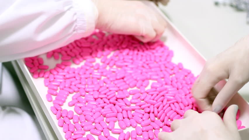 Technicians inspecting the quality of pills at a pharmaceutical plant.
