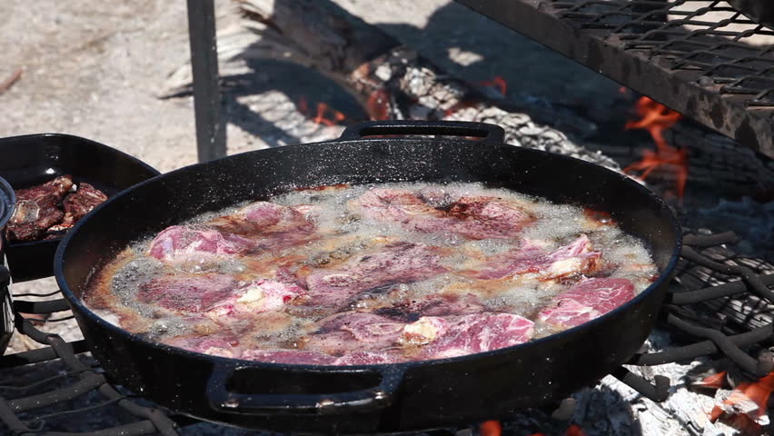 Lamb chop steaks and Mutton cooking in cast iron pans over an open outdoor fire. Cowboy and sheep camp bbq and party. Fresh meat with smoke and oil boiling near Dutch Oven.