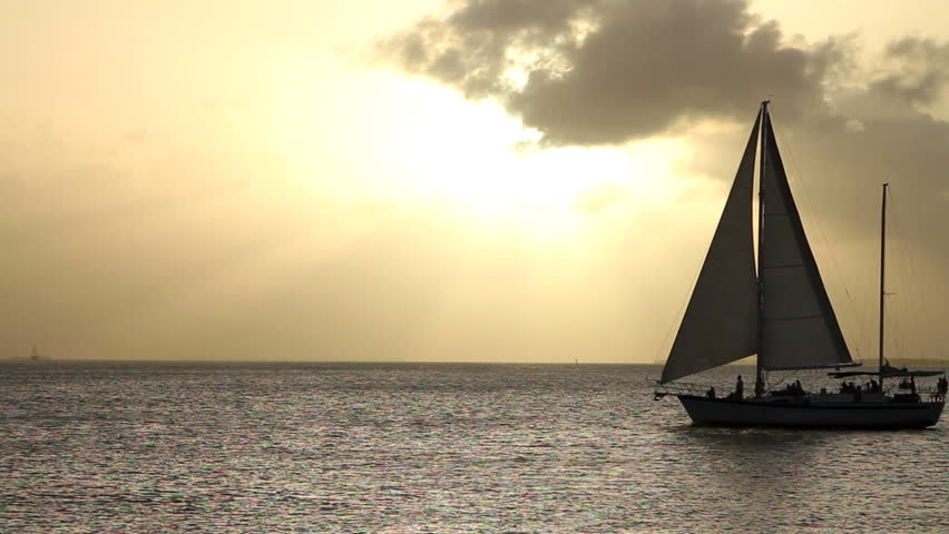 Silhouetted sailboat moves across the water in front of the setting sun in Key West, Florida.