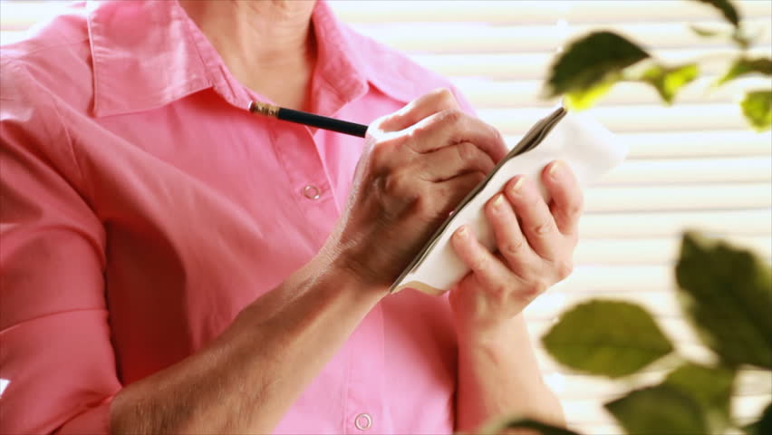 An older woman writing on a tablet stops and becomes concerned about the pain she is experiencing in her fingers due to arthritis.