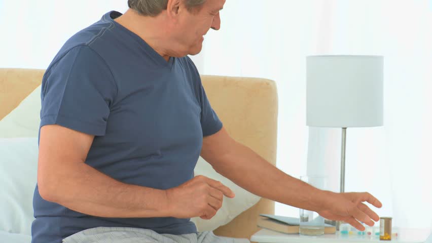 A sick man taking his pills in his bedroom