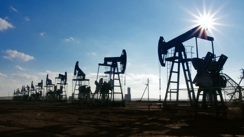 working oil pumps silhouette against sun