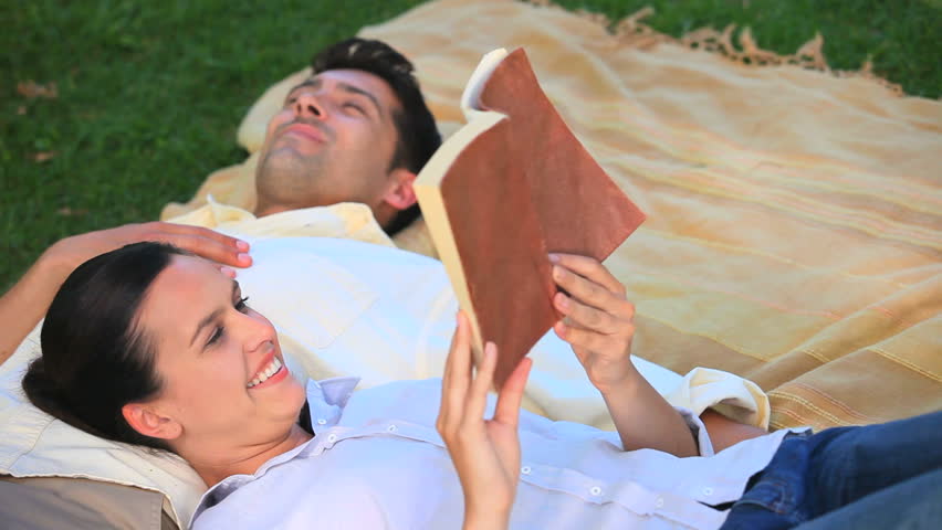 Woman reading a book in a park while her husband taking a nap