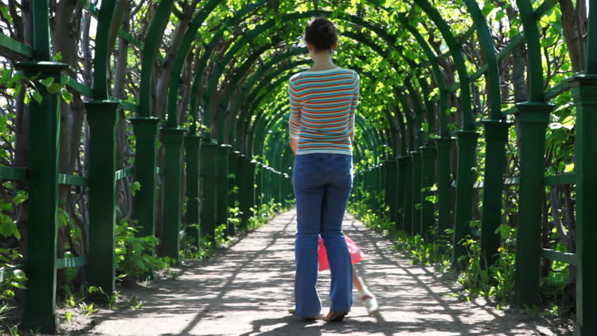 happy mother and little daughter spin holding hands in arched corridor braided green plants by spring day