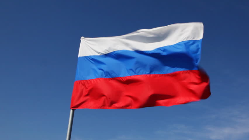 big Russian tricolor flag flutters in wind against blue sky
