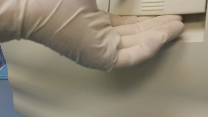 Technician, wearing gloves, opens autoclave, inserts medical, surgical instruments, laid out on trays to be sterilized, closes door. 1080p