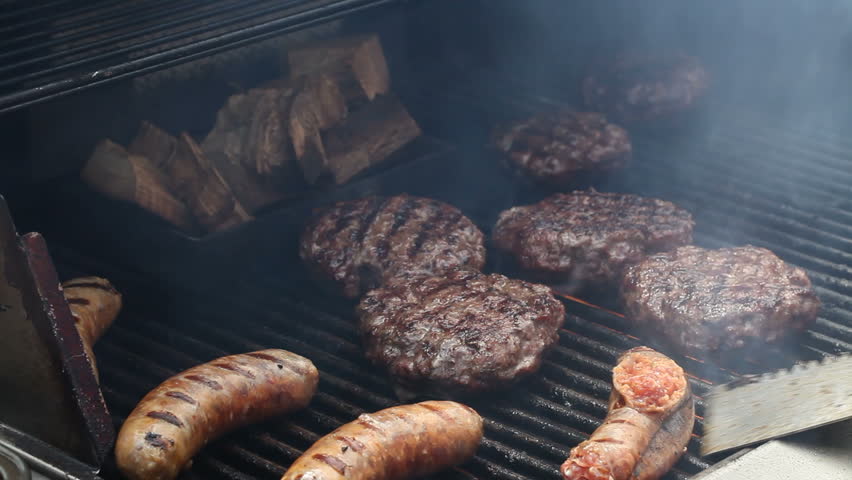 A barbecue scene with chicken meat, burgers and sausages while flipped over with a tong spatula turner  on the grill over a calm fire flame.