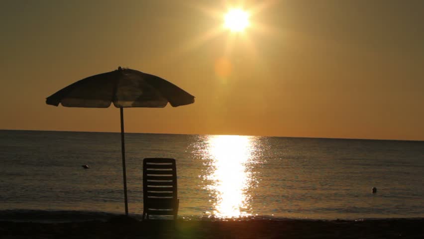 Deckchair stand under parasol on beach, woman passed from left to right and made photo of sunset on phone