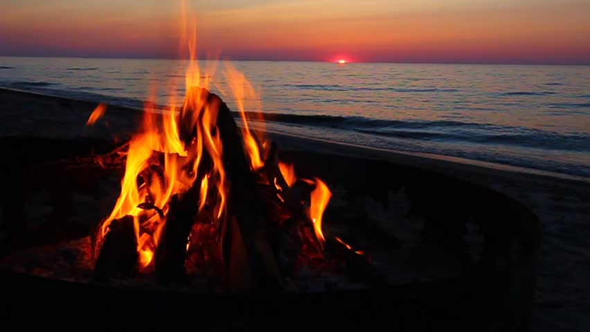 Campfire burns brightly at sunset along the beautiful beach of Lake Superior in northern Michigan