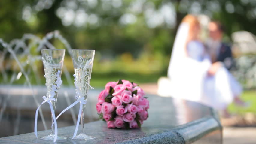 bridal bouquet and two glasses of champagne near the fountain in the background newlyweds