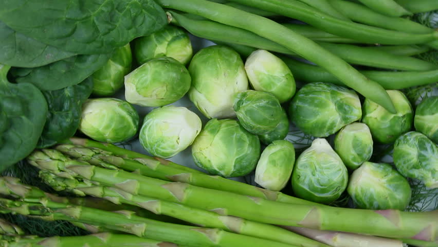 Fresh, organic asparagus, green beans, spinach and Brussels sprouts rotate on white plate background. 1080p