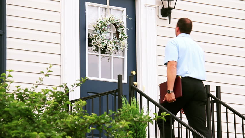 A door to door salesman walks up to a house and knocks on the door.