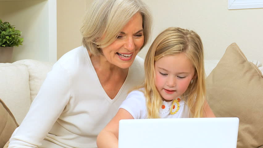 Proud grandma hugging her cute grandchild after watching her play on laptop