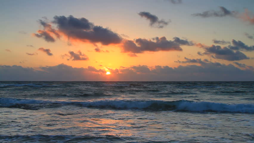 The golden glow of the sun rising over the Gulf of Mexico with rolling waves and beautiful clouds in Cancun, Mexico.