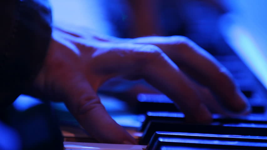Close up of hands playing a keyboard in a creepy lighting setup.  Looks like lightning is striking while he plays.