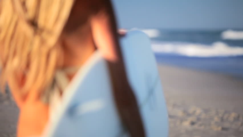 Beautiful slim blonde girl in a bikini walking to the waves with a surfboard