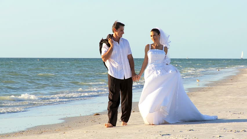 Bride & bridegroom walking barefoot on the beach after their wedding ceremony filmed at 60FPS