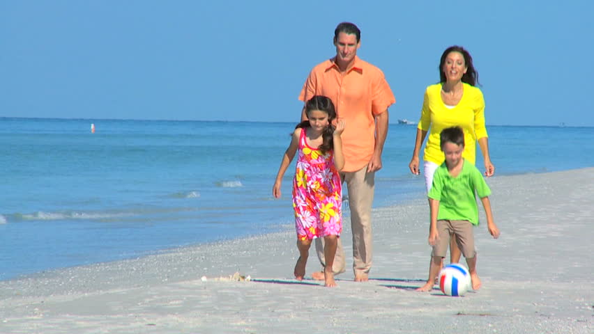 Healthy young family having fun kicking a ball on the beach filmed at 60FPS