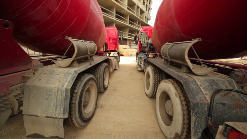 Two concrete mixer stand near unfinished tall high-rise buildings, upward camera movement