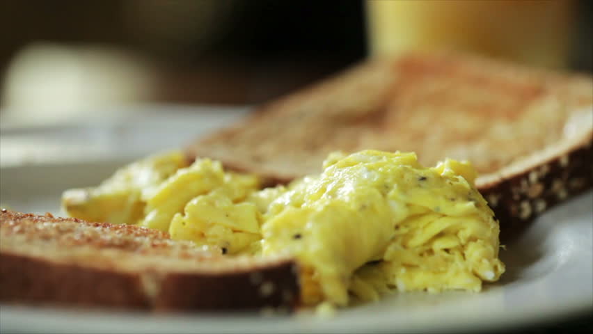 A woman who is eating a typical American breakfast of eggs, toast, and orange juice. Shallow DOF, limited focus area
