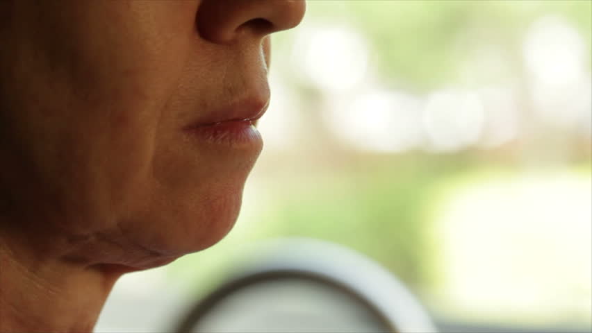 A close up of a mature woman standing in front of a window taking her prescription medication.