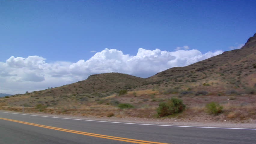 A two lane blacktop highway slices through mountains.