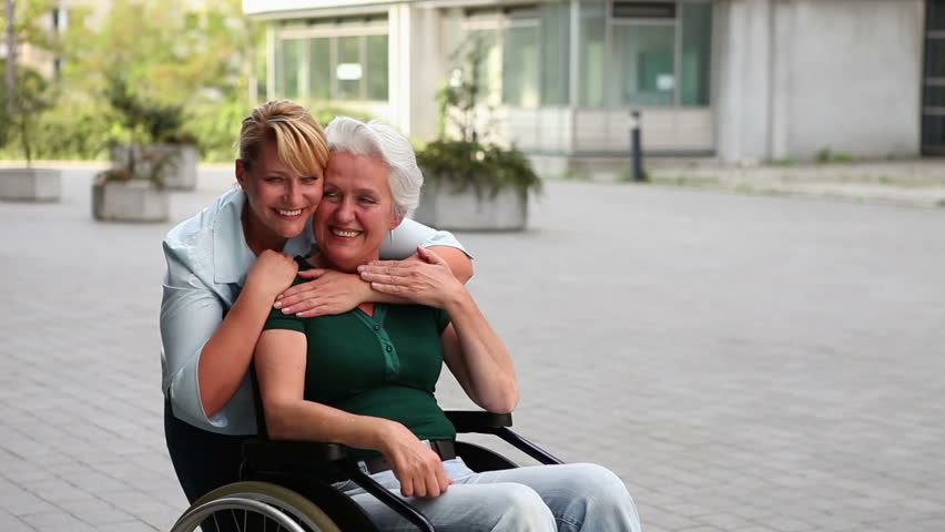 Disabled woman in wheelchair and her nurse holding thumbs up