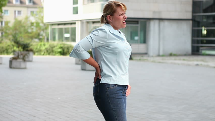 Woman in city with back pain holding her hand to her hips