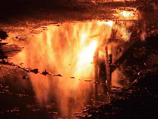 Reflections of flames in a puddle of water with firemen walking by.