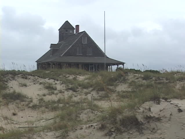 A black beach house rests at the top of a sandy hill.