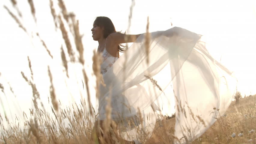 A woman waves a sheer white sheet while moving around a wheat field.