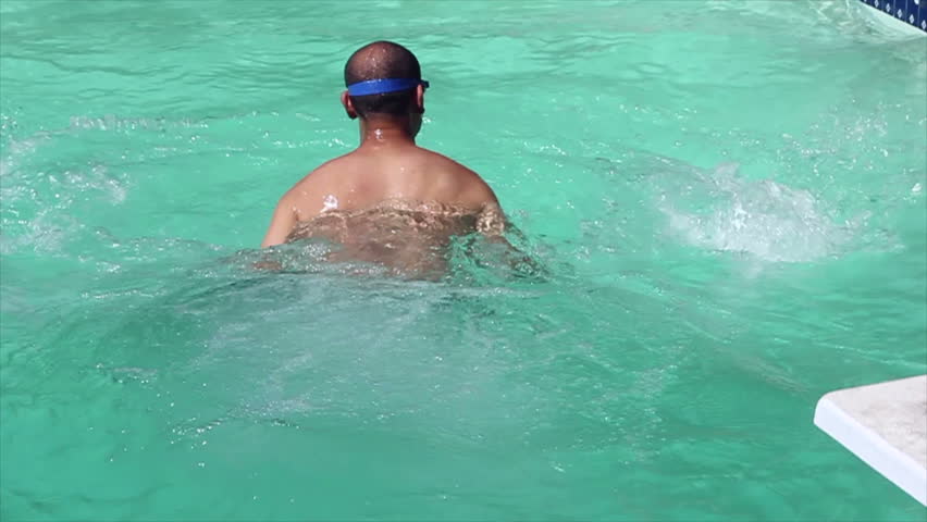 Slow motion HD footage of an Asian man with goggles jumping cannon-ball style into a pool, while facing forward