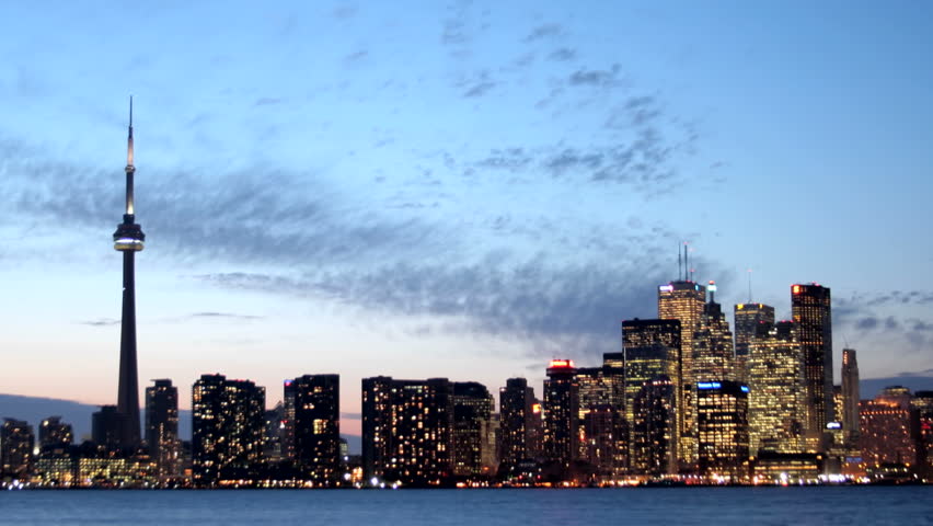 The lights of the Toronto skyline glow brighter under a colorful darkening sky.
