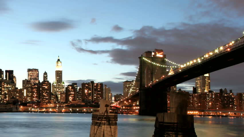 Slow pan of a time-lapsed view of the Brooklyn Bridge and the New York City skyline from golden-hour to night.