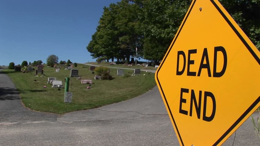 A dead end sign near a cemetery on a hillside.