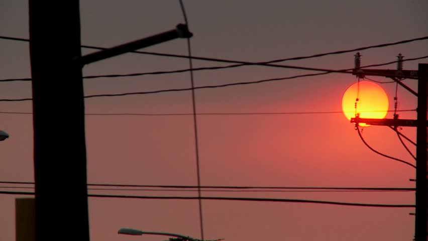 A orange ball of sun sets behind power lines during fire season in California.