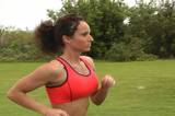 A pretty brunette with remarkable muscle definition jogging outdoors.  Tracking shot, side view.