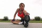 A pretty brunette in fitness wear, with remarkable muscle definition, stretches prior to jogging outdoors.  Low angle.