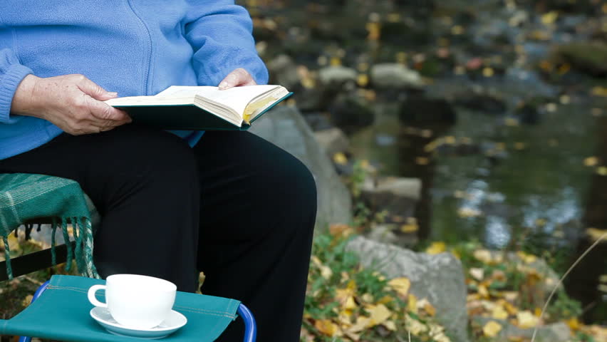 Elderly woman reading a book with a cup of coffee in the park. Unrecognizable Person,  Side View