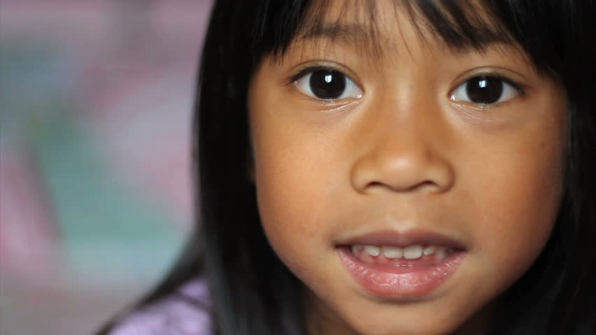 A cute little 5 year old Asian girl wiggles her first loose front tooth.