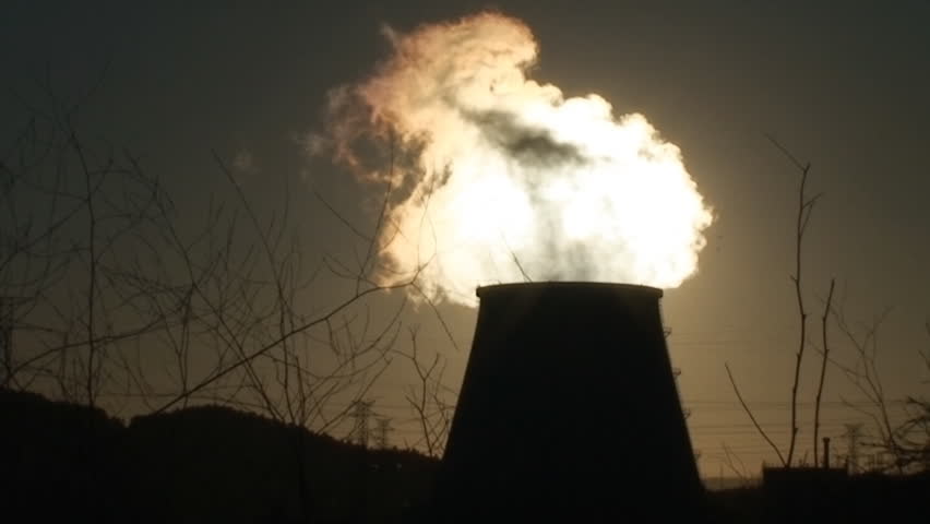 Chimney of power plant against sun, cooling towers emitting much pollution