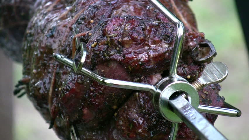 detail of savory meat roasting on a spinning rotisserie with smoke, dripping juices, and flame reflections