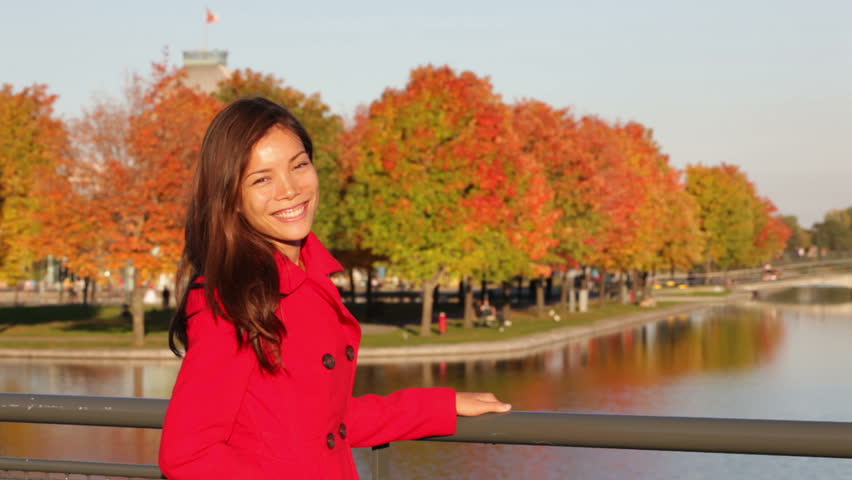 Fall woman smiling at camera and looking around with autumn colored trees. Beautiful mixed race Asian Caucasian female model in Old Port, Montreal, Quebec, Canada.